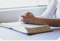 Hands resting in prayer over an open Bible
